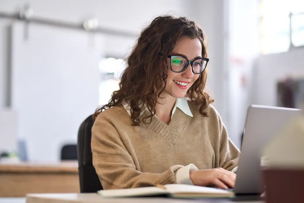 Junge Auszubildende sitzt am Schreibtisch mit Laptop